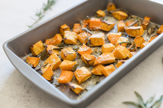 Baking sheet/frying pan with oven baked butternut squash/pumpkin with sage leaves and shredded parmesan cheese. Shallow space, close up, background. 