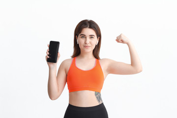 Young fitness woman posing isolated on a white background listening to music with wireless headphones.