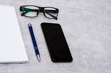 Blank notepad with blue pen and smartphone and glasses flat lay. View on stationery with mobile phone and spectacles. Art, business, creation, imagination, office supplies and business concept.