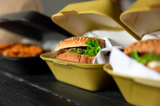Hamburger in a takeaway container on the wooden background. Food delivery and fast food concept