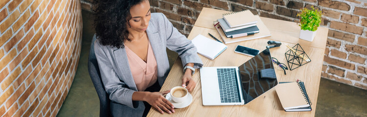 Panoramic shot of African American Casual businesswoman with coffee cup and laptop at desk