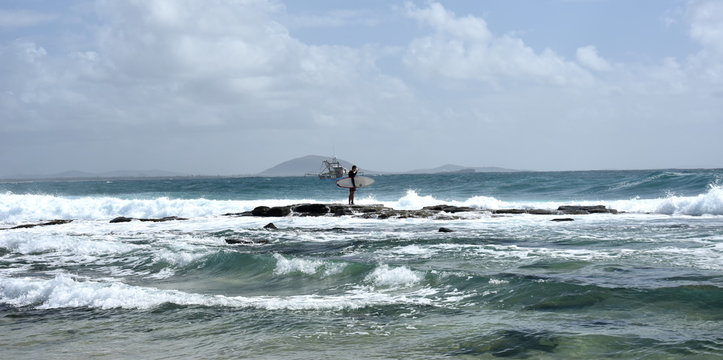 A surfer guy waiting for big waves, surboard in his hand. Beautiful weather at Buddina Beach along Pacific Boulevard (Sunshine Coast, Queensland, Australia).