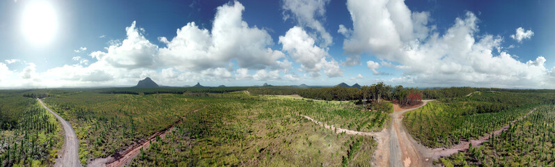 Fototapeta na wymiar Panoramic aerial view of Glass House Mountains National Park on Sunshine Coast (Queensland, Australia). The Glasshouse Mountains are silhouetted in the afternoon sunlight.