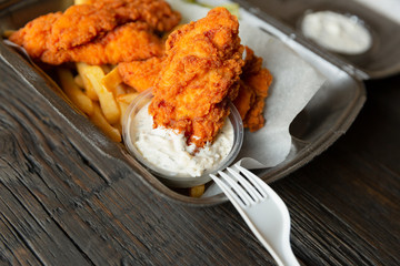 Fried chicken and french fries and in a takeaway container on the wooden background. Food delivery and fast food concept