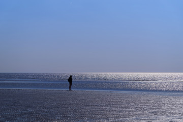 Silhouette of single human on the beach looking towards horizon