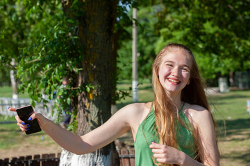 Beautiful young woman with blue eyes on a green background. Wistful young woman on a street in a park in the background.