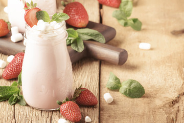Strawberry milkshake with fresh berry and green mint, decorated marshmallows, summer drink, wood old background, selective focus