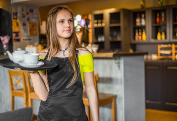 Fototapeta na wymiar Portrait young waitress standing in cafe. girl the waiter holds in bunches a tray with utensils. Restaurant service