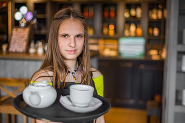 Portrait young waitress standing in cafe. girl the waiter holds in bunches a tray with utensils. Restaurant service