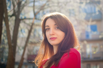 Obraz premium Attractive brunette girl is enjoying spring outdoors and looking at tne camera on building background