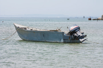 Obraz premium Old fishing boat with motor on the coast and in the sea water in summer.