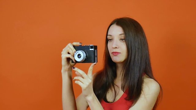 Beautiful young brown-haired girl with a camera in hand. Emotions. Art portrait in a studio on an orange background