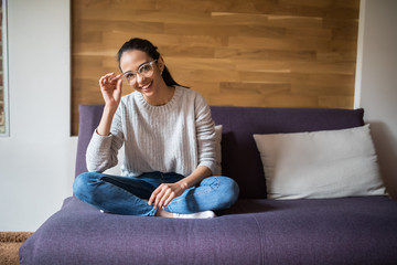 Obraz premium Beautiful young cheerful woman in glasses looking at camera with smile while sitting on the couch at home