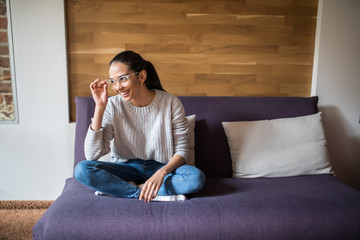 Obraz premium Beautiful young cheerful woman in glasses looking at camera with smile while sitting on the couch at home