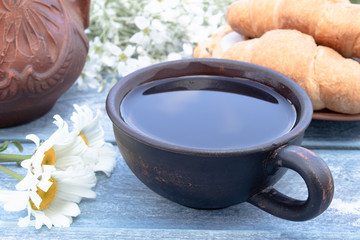 Next to the croissants and daisies is a cup of tea.