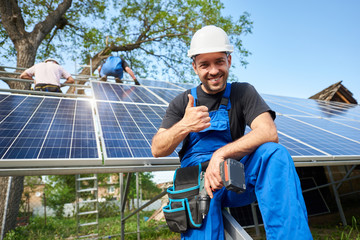 Portrait of smiling technician with electrical screwdriver showing thumb-up in front of unfinished...