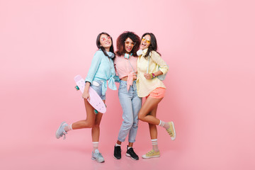 Full-length portrait of skater girl posing with best friends on pink background. Indoor photo of...