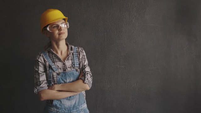 young woman builder in a yellow helmet with protective glasses on her face