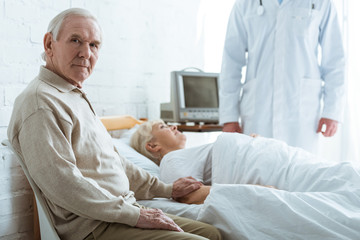 cropped view of doctor, senior man and sick senior woman lying on bed in hospital