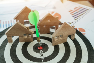 Dart arrow or dartboard hitting on number target center with miniature wooden house models. Success...