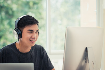 Student learning online study concept: Asian Young man listening with Headphones and laptop, sitting holding smartphone chatting in home for e-learning in educational technology by self