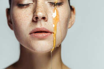 Closeup portrait of beautiful young brunette woman with freckles and honey on face with closed eyes...