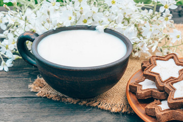 Next to the cookies and white flowers is a cup of milk on a napkin.