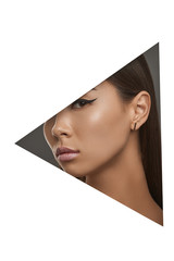 Cropped side geometric portrait of woman with black flicks. The young girl with dark hair is wearing golden stud earrings in the shape of thin rectangle, looking at camera behind triangle foreground.
