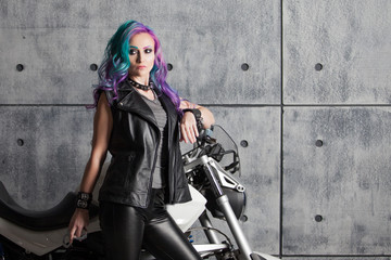 Naklejka na ściany i meble Biker chick in front of motorcycle. Beautiful and pert young woman in leather clothes