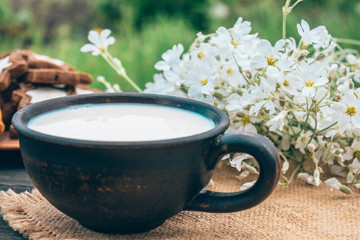 Next to the cookies and white flowers is a cup of milk on a wooden table.