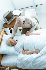 Obraz na płótnie Canvas overhead view of senior man stroking wife in coma in clinic