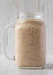 Homemade banana, kiwi, apple smoothie in a glass jar mug over white wooden surface, side view. Close-up.