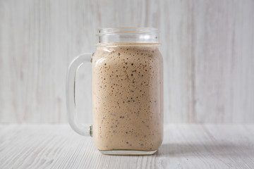 Homemade banana, kiwi, apple smoothie in a glass jar mug over white wooden background, side view. Close-up.