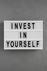 'Invest in yourself' words on a modern board over gray background, top view. Overhead, flat lay, from above. Close-up.