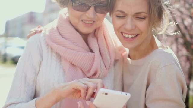 Two women discussing photos in the smartphone. Spring portrait in the park. Network marketing, MLM business