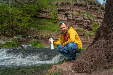 Man drinking coffee from white thermos near mountain river