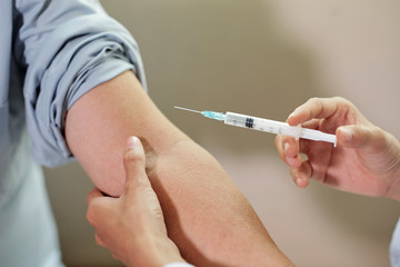 Close-up of doctor holding syringe and is going to do an injection in the arm of the patient at...