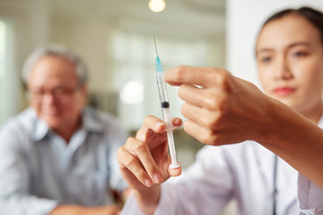 Close-up of female doctor preparing syringe for vaccination from flu for senior man who sitting in...
