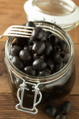 Black olives isolated, mason jar, wooden background. Mediteranian foods.