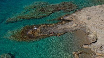 Aerial drone photo of iconic deep turquoise beach of Latinaki with crystal clear sea and rocky sea shore forming small caves, Folegandros island, Cyclades, Greece