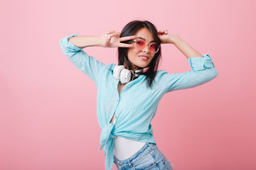 Close-up portrait of stylish asian young woman wears elegant glasses and cotton shirt. Indoor photo of adorable hispanic girl with black shiny hair relaxing in pink room.