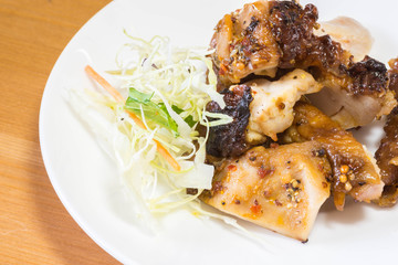 Chopped grilled chicken breast barbecue in a white plate saucer with green leafy vegetables on the side as garnish.