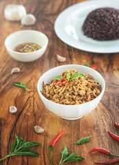 Stir fried basil with minced pork in a bowl and rice berries on the plate. put on a wooden table