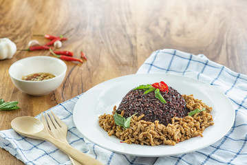 Stir fried basil with minced pork and berry rice in a plate on a wooden table.