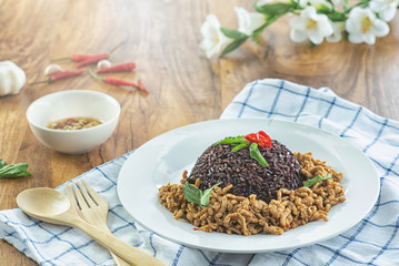 Stir fried basil with minced pork and berry rice in a plate on a wooden table.