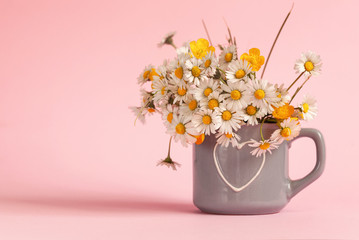 A bouquet of field daisies in a mug on a pink background. Happy Birthday or Holiday concept.
