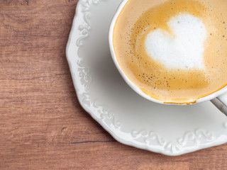 Vintage white coffee cup with heart shape latte art on wood table.