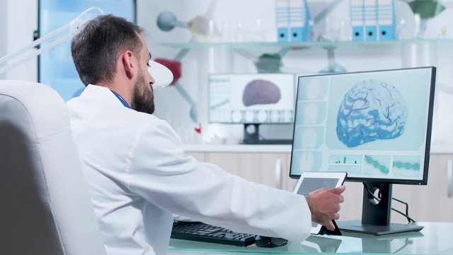 In modern research facility doctor is looking at X ray scans on a digital tablet PC. 3D brain simulation is running on the computer screen