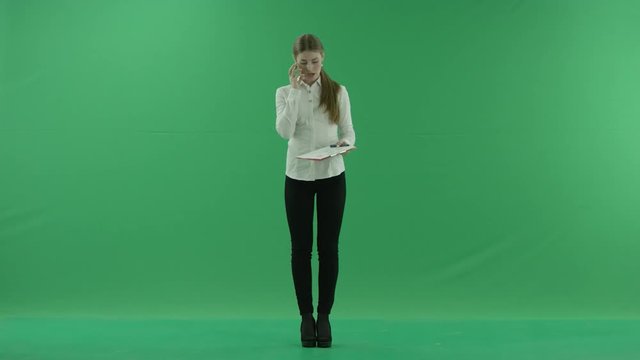 A young girl is talking on her phone and writing something into her clipboard on the green screen