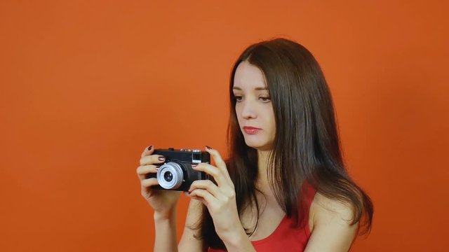 Beautiful young brown-haired girl with a camera in hand. Emotions. Art portrait in a studio on an orange background